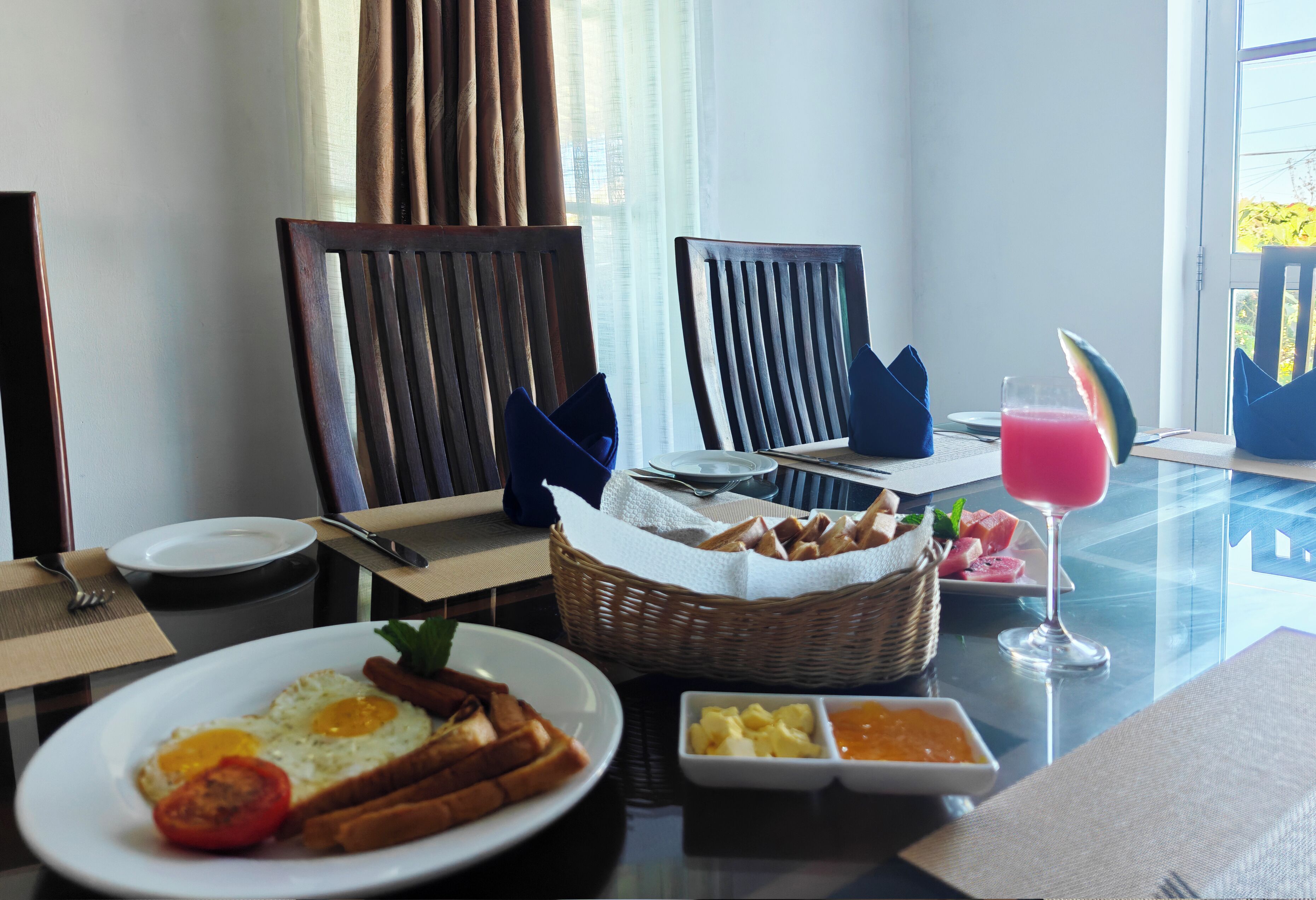A breakfast setting with plates of food, a glass of drink, and a basket of bread.