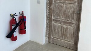 A hallway with a wooden door and two red fire extinguishers mounted on the wall. - Ahadi Beachfront 2 Bedroom by YourHost (Mtwapa)