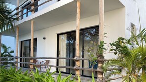A two-story building with a balcony, stone wall, and tropical plants. - Ahadi Beachfront 2 Bedroom by YourHost (Mtwapa)