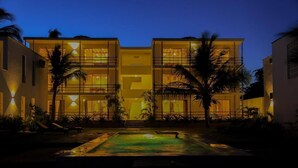 A multi-story hotel with a pool in the foreground, surrounded by palm trees and well-lit by ambient lighting. - Ahadi Beachfront 2 Bedroom by YourHost (Mtwapa)