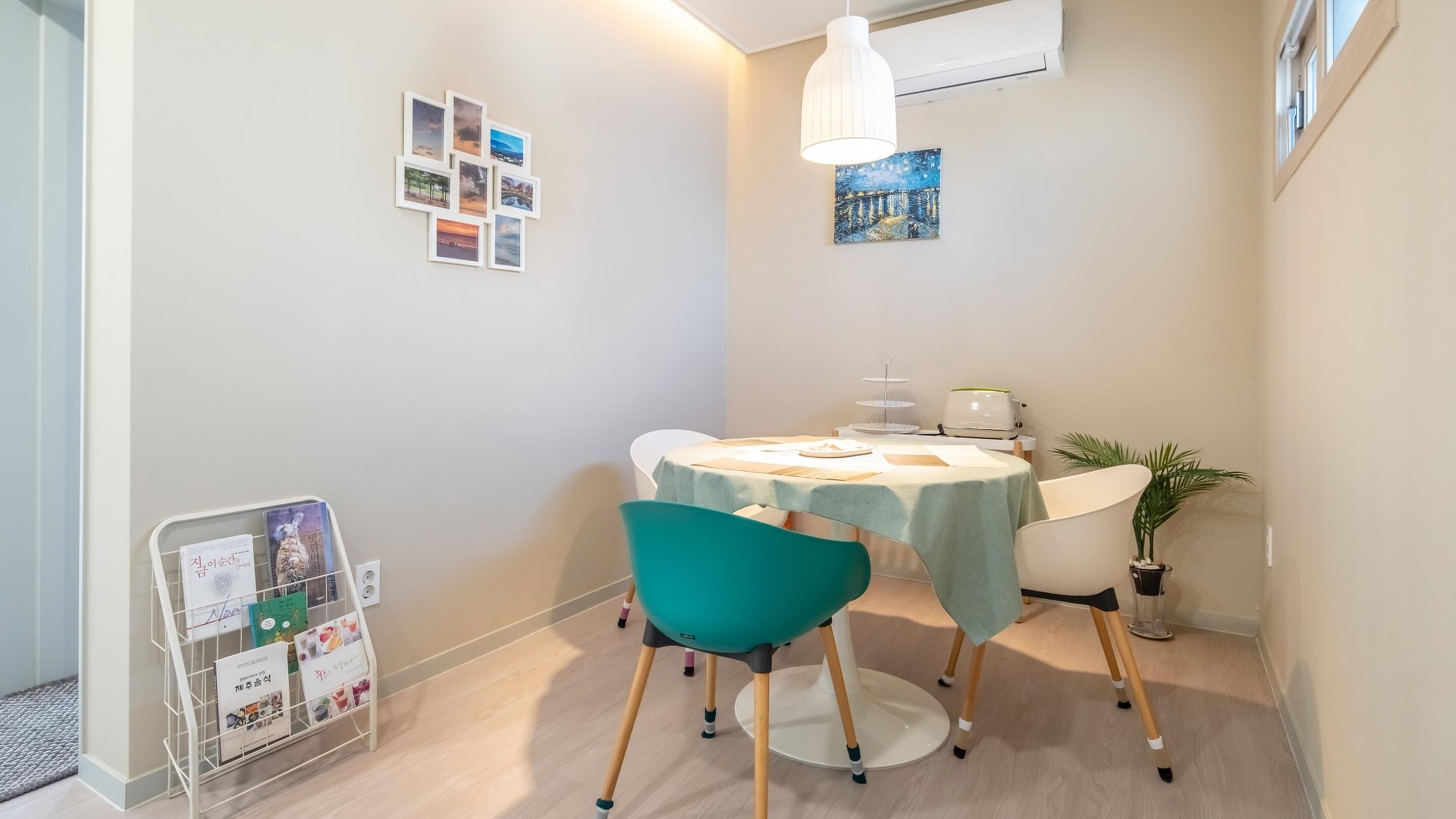 Una habitación pequeña y acogedora con una mesa redonda, sillas color turquesa, una lámpara blanca y una planta pequeña.