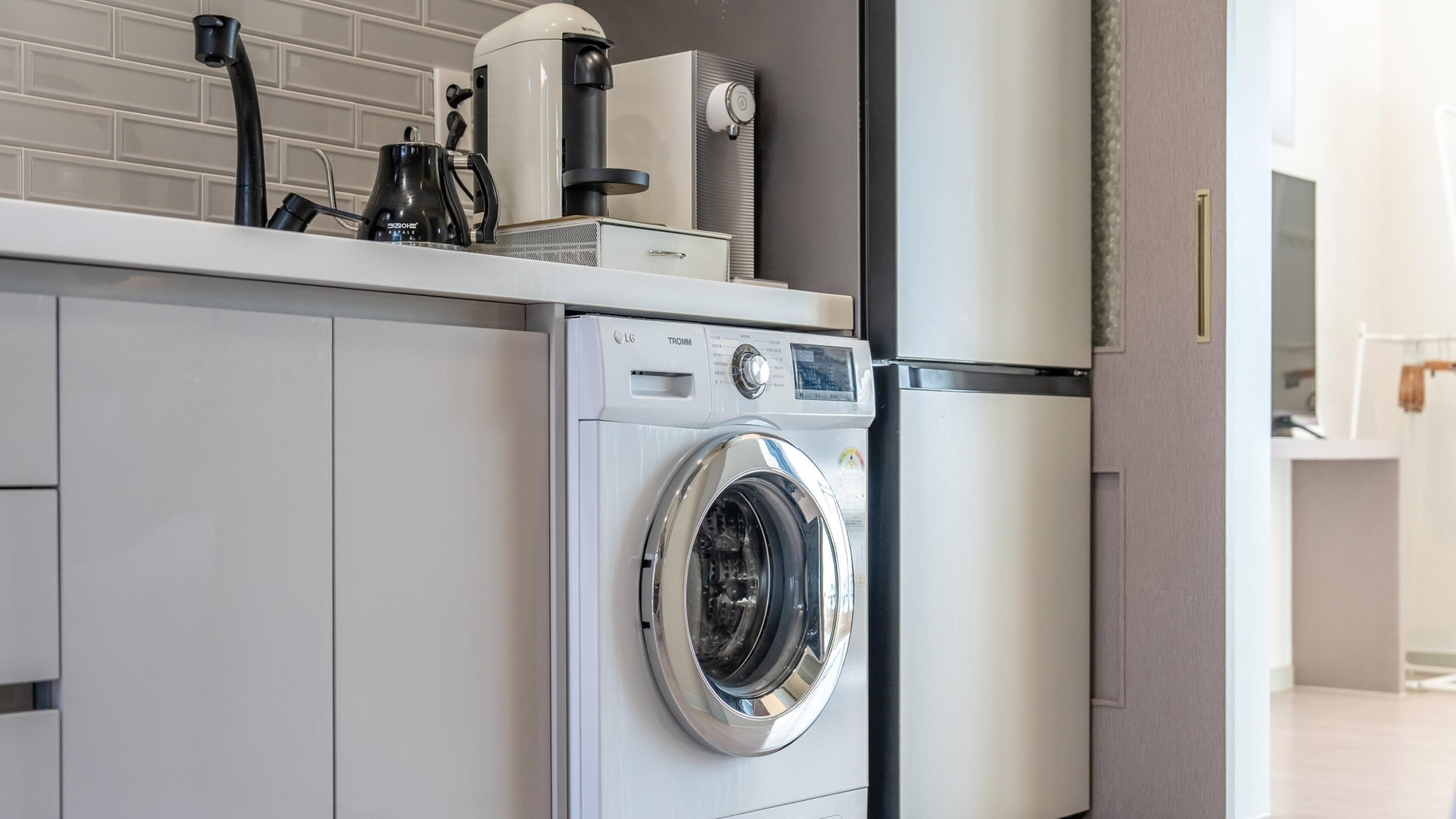 Una cocina moderna con lavadora y secadora integradas, una cafetera y un hervidor sobre la encimera.