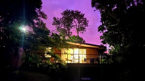 A house with a large window, surrounded by trees, under a purple sky. - Surfers shack - peaceful & minutes walk to the beach in stunning Nambucca (Nambucca Heads)