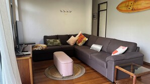 A modern living room with a grey sofa, a small ottoman, a wooden coffee table, and a flat-screen TV on a stand. - Surfers shack - peaceful & minutes walk to the beach in stunning Nambucca (Nambucca Heads)