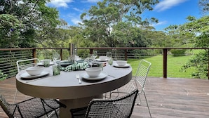 A round table set for dining on an outdoor deck with chairs, surrounded by lush greenery and trees. - Surfers shack - peaceful & minutes walk to the beach in stunning Nambucca (Nambucca Heads)