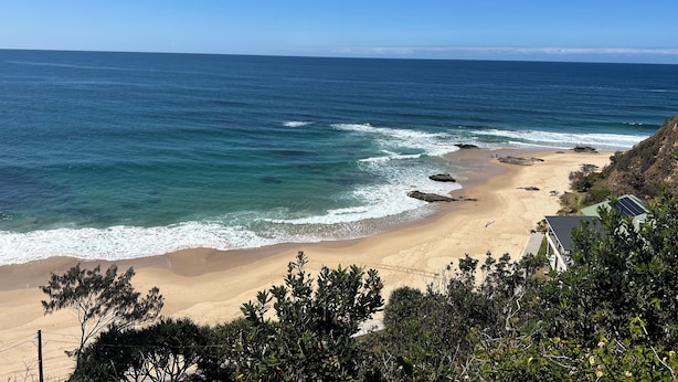 A beach with clear blue water, sandy shore, and some vegetation in the foreground. - Surfers shack - peaceful & minutes walk to the beach in stunning Nambucca (Nambucca Heads)
