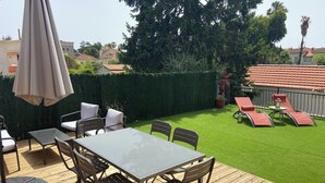 A wooden deck with a glass-top table and chairs, surrounded by a well-maintained lawn and a hedge. - Appartement 3 Chambres + Terrasse de 60 m2 Au1er Étage D'une Villa à Golfe Juan (Vallauris)