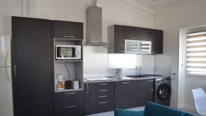 A compact kitchen with dark cabinetry, a microwave, a coffee maker, a sink, and a washing machine. - Appartement 3 Chambres + Terrasse de 60 m2 Au1er Étage D'une Villa à Golfe Juan (Vallauris)
