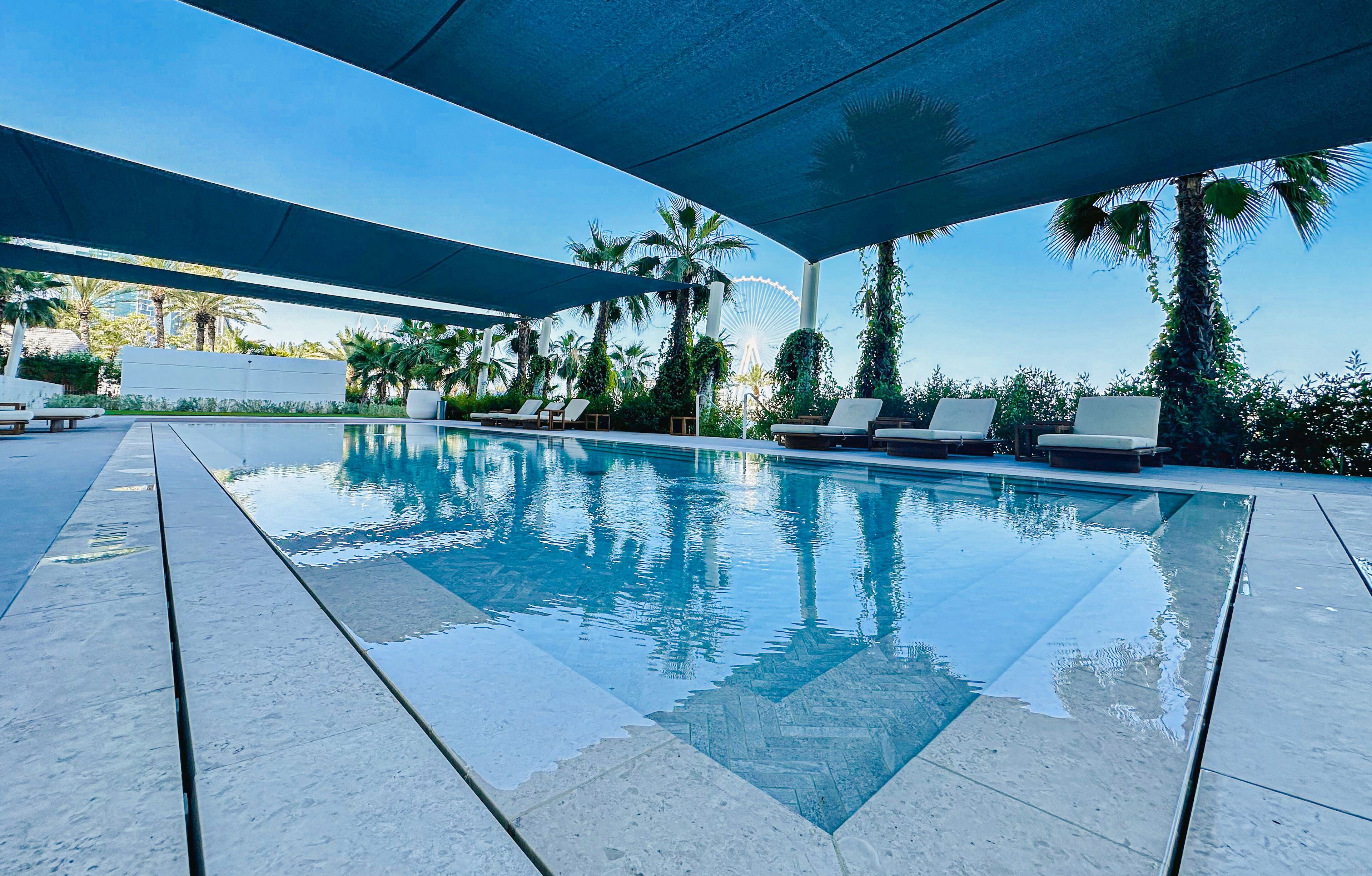 Un espace piscine avec une eau d’un bleu limpide, des chaises longues et des palmiers.