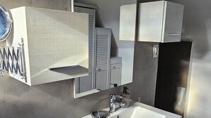 Une salle de bain moderne avec un grand miroir, un lavabo blanc et des meubles de rangement gris.