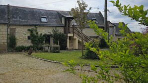 Une maison en pierre avec une allée en gravier, un escalier en bois et un petit jardin.