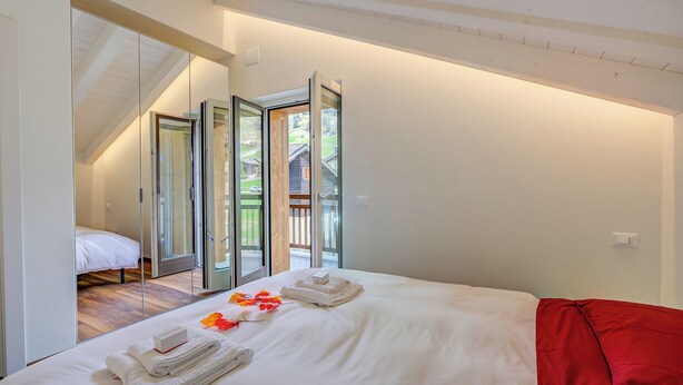 Une chambre à coucher avec un lit, une couverture rouge et une porte vitrée donnant sur un balcon.