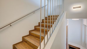Un escalier moderne avec des marches en bois et des rampes en métal, menant à l’étage supérieur.