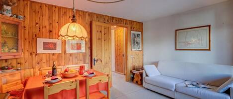 A wooden-paneled room with a dining table, chairs, a white sofa, and a hanging lamp.