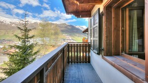 A balcony with a wooden railing, a view of a mountain range, and a building with large windows. - Casa Ciuk (Livigno)
