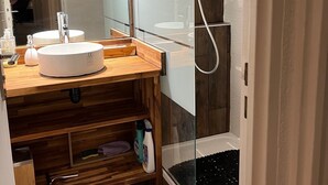 Een moderne badkamer met een houten wastafelmeubel, een douchecabine met glazen wanden en een grote spiegel.