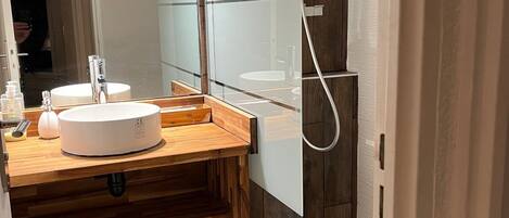 A modern bathroom with a wooden vanity, a glass shower enclosure, and a large mirror.