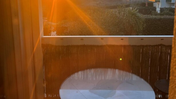 Een kamer met een groot raam met uitzicht op een zonsondergang, een ronde tafel en een hanglamp.