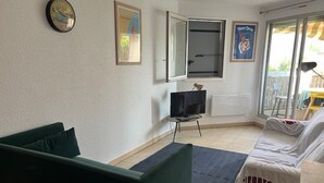 Een kamer met een groene bank, een bed met witte beddengoed, een televisie op een standaard en een raam met uitzicht op het omliggende landschap.