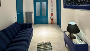 Un pasillo con un sofá azul, un tapete estampado, un banco azul y una lámpara fijada a la pared.