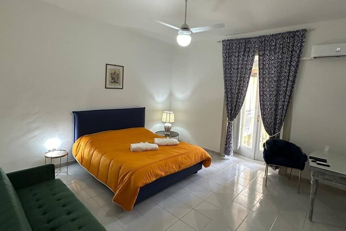 A bedroom with a bed, a green sofa, a desk, a ceiling fan, and a window with curtains.