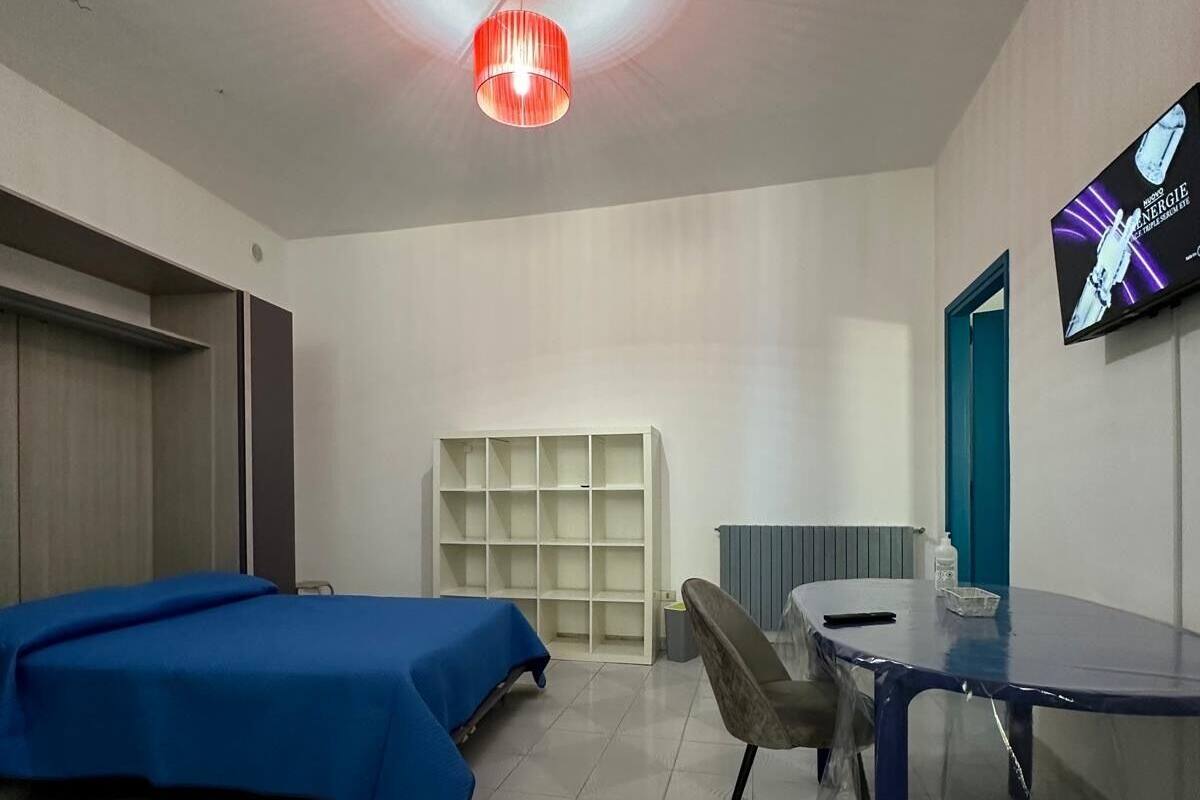 A hotel room with two beds, a desk, a chair, a TV, and a shelf.