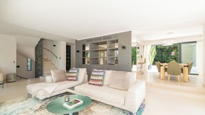 A modern living room with a sectional sofa, a glass coffee table, and a dining area with a cactus plant.