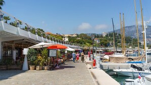 A marina with boats docked, a paved walkway, and outdoor seating areas with umbrellas.