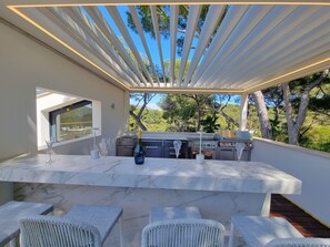 An outdoor kitchen area with a marble countertop, white wicker chairs, and a view of trees and sky.