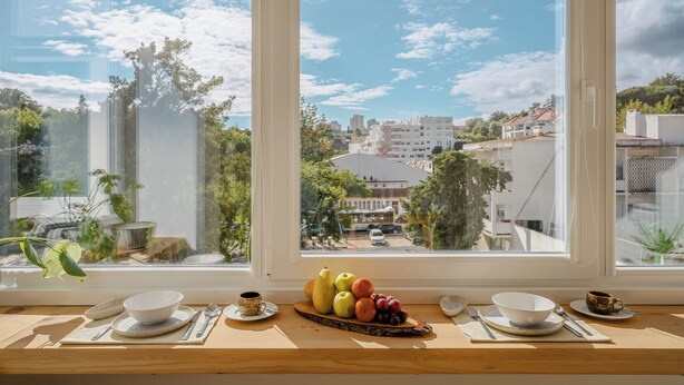 Ein Esstisch mit Früchten und Schalen, ein Fenster mit Blick auf Gebäude und Bäume.