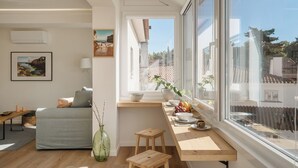 Ein helles Wohnzimmer mit einer Couch, einem hölzernen Hocker, einem Esstisch mit Obst und Blick ins Freie.