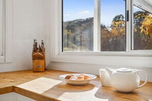 Un plan de travail de cuisine avec une planche à découper en bois, un bol d’œufs, une théière blanche et un bloc à couteaux.