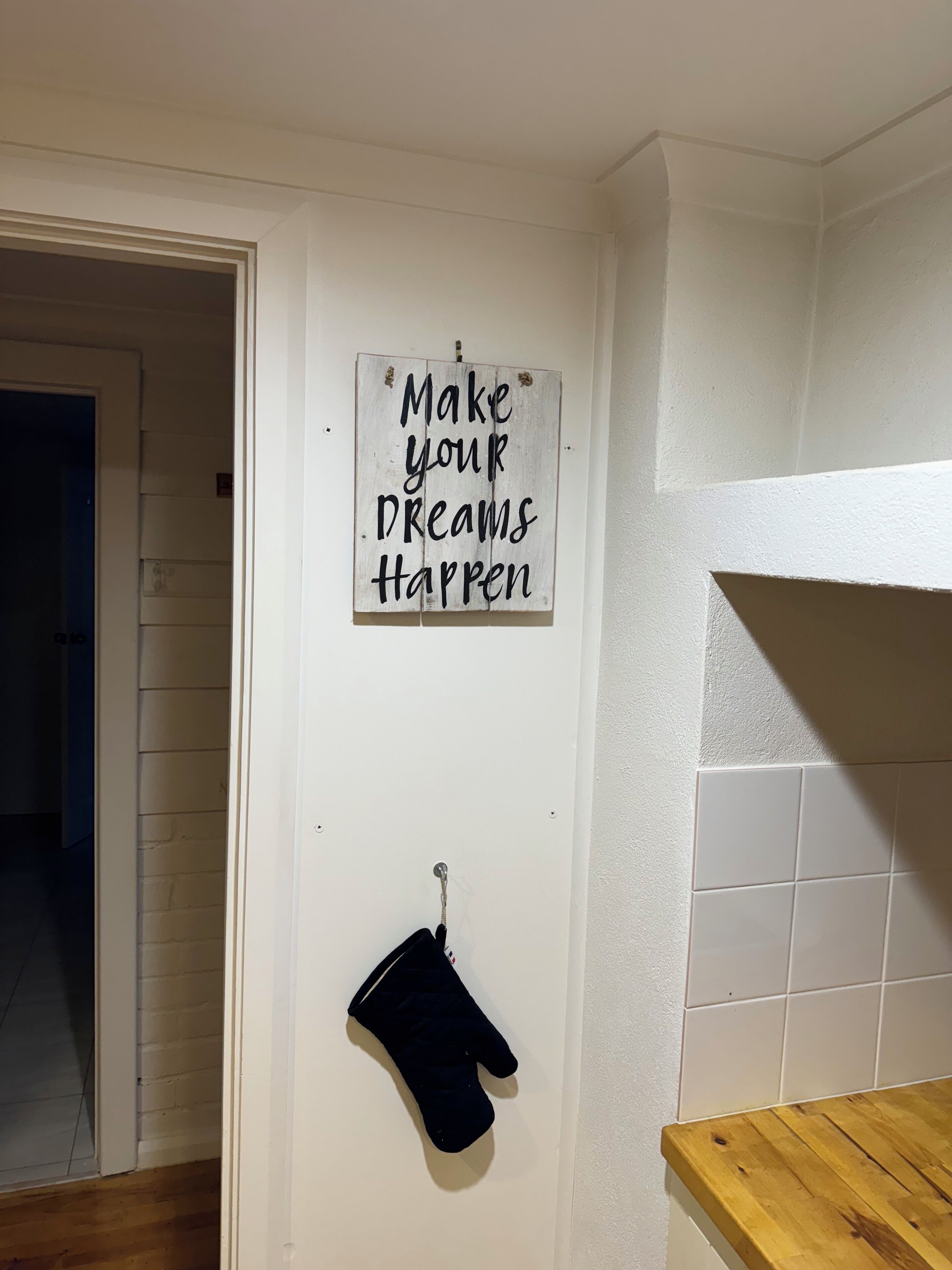Eine Küche mit einer Holzauslage, einem aufgehängten schwarzen Topflappen und einem motivierenden Spruch an der Wand.