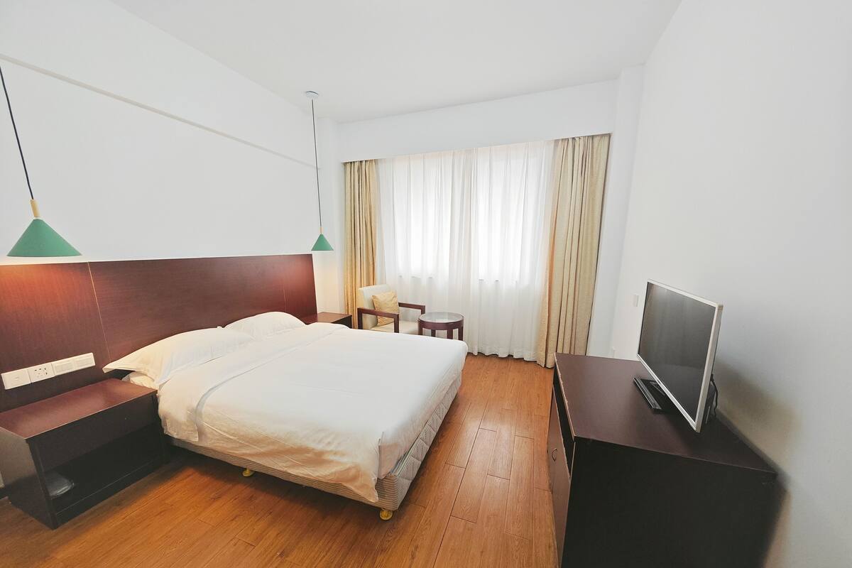 Una habitación de hotel con cama, mesita de noche, lámpara, televisión y cortinas.