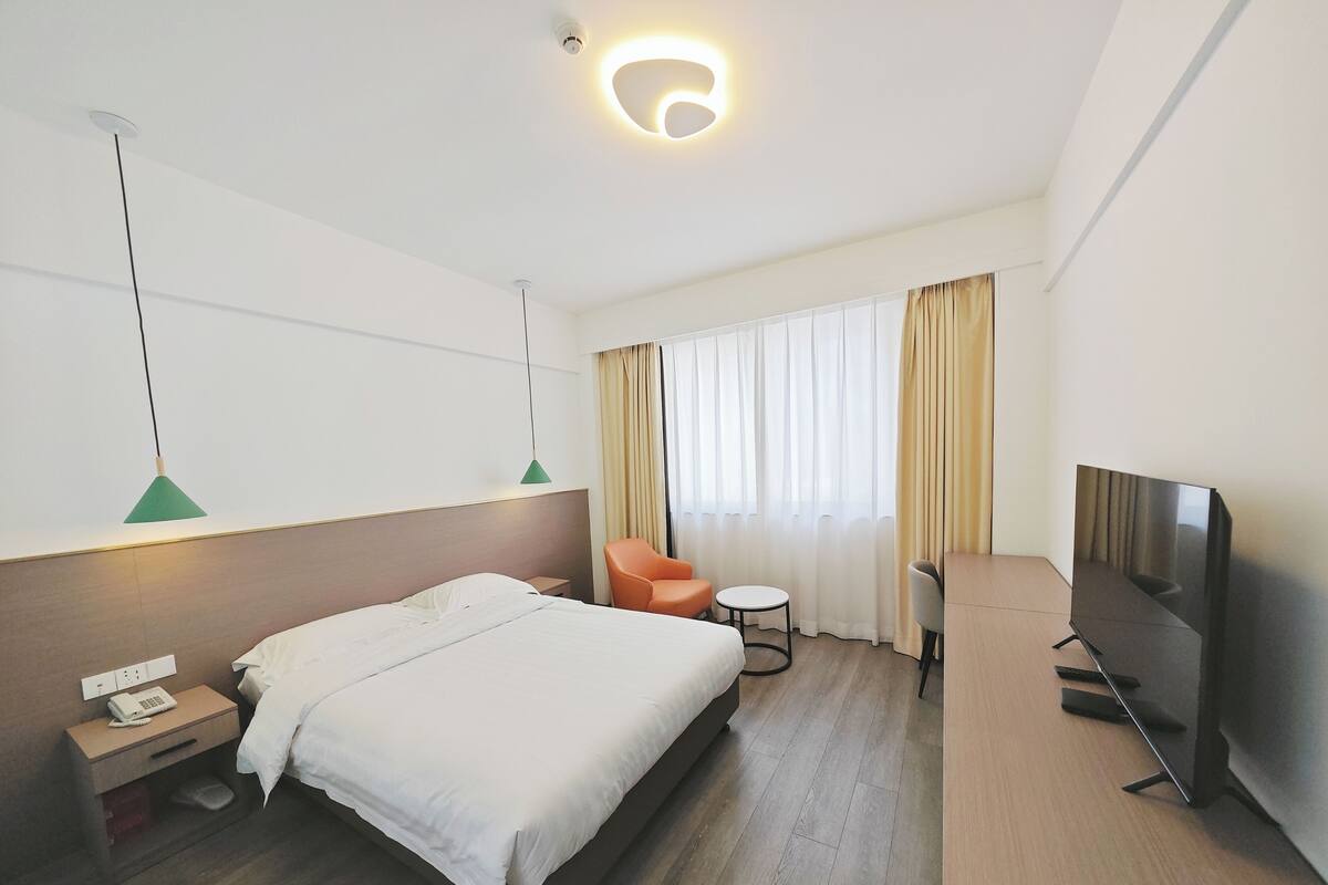 Habitación de hotel con cama, escritorio, silla, televisor y ventana con cortinas.
