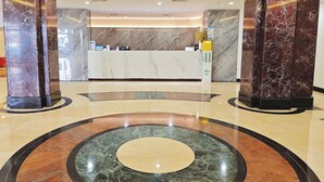 Un hall d’hôtel agrémenté de colonnes en marbre, d’un comptoir d’accueil et d’un motif circulaire en marbre sur le sol.