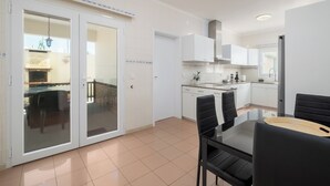 A modern kitchen with white cabinets, a dining area with black chairs, and a glass door leading to an outdoor patio.