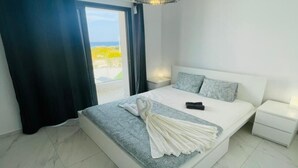 A modern bedroom with a large bed, a chandelier, a nightstand, and a view of the outdoors. - By the Beach Villa Natalya (Protaras)