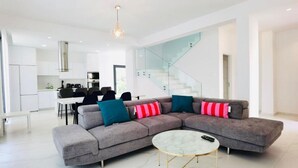 A modern living room with a grey sectional sofa, a marble coffee table, and a glass staircase. - By the Beach Villa Natalya (Protaras)