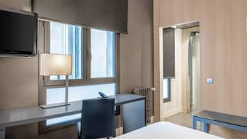 A hotel room with a bed, a desk, a chair, a TV, and a window.