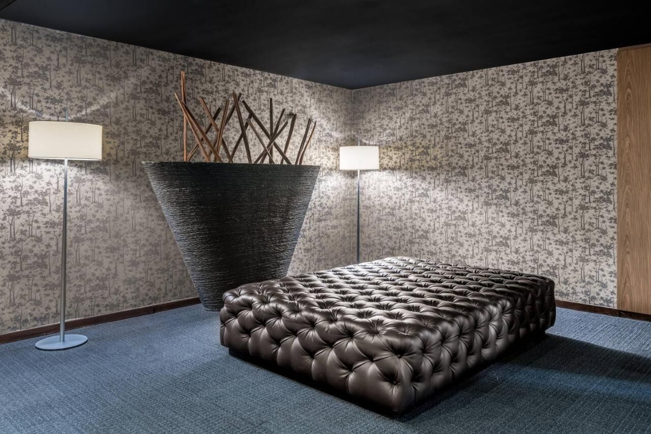 Ein Schlafzimmer mit einem gepolsterten Lederbett, einer großen Vase mit Zweigen und zwei Wandlampen.