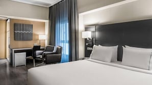 Une chambre d’hôtel avec un grand lit, un bureau avec une chaise, une petite table de travail, une lampe et un téléviseur fixé au mur.