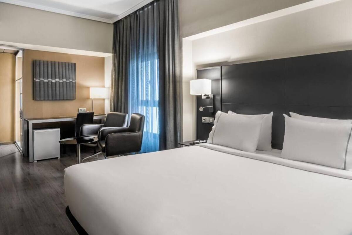 Une chambre d’hôtel avec un grand lit, un bureau avec une chaise, une petite table de travail, une lampe et un téléviseur fixé au mur.