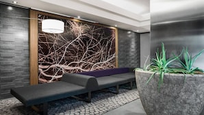 Un espace de détente moderne comprenant un banc, une grande plante en pot et un mur orné d’un motif représentant une branche d’arbre.