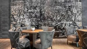 Un intérieur moderne avec une table ronde et quatre chaises grises, une grande peinture abstraite au mur et un coin bar avec des bouteilles.