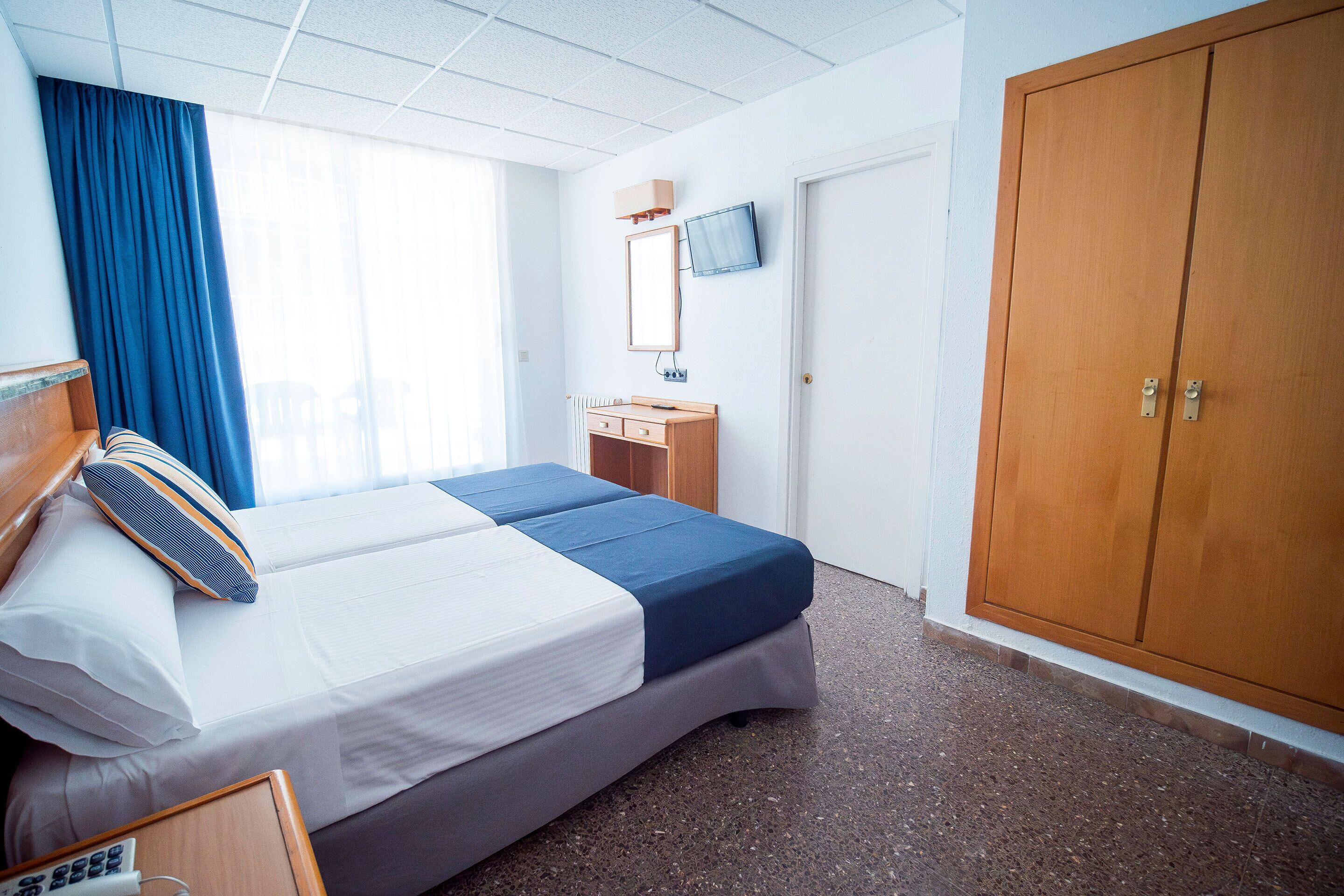 A hotel room with a bed, a desk, a television, and a wardrobe.