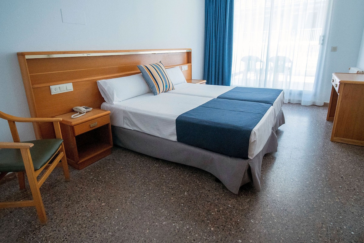Habitación de hotel con cama doble, mesita de noche con teléfono, una silla y un escritorio de madera pequeño.
