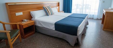 A hotel room with a double bed, a bedside table with a phone, a chair, and a small wooden desk.