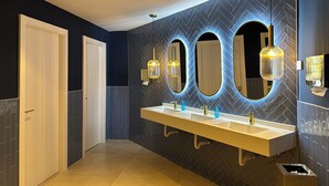 Een moderne badkamer met een wand in herringbone patroon, een grote spiegel en een wastafel met drie wasbakken.