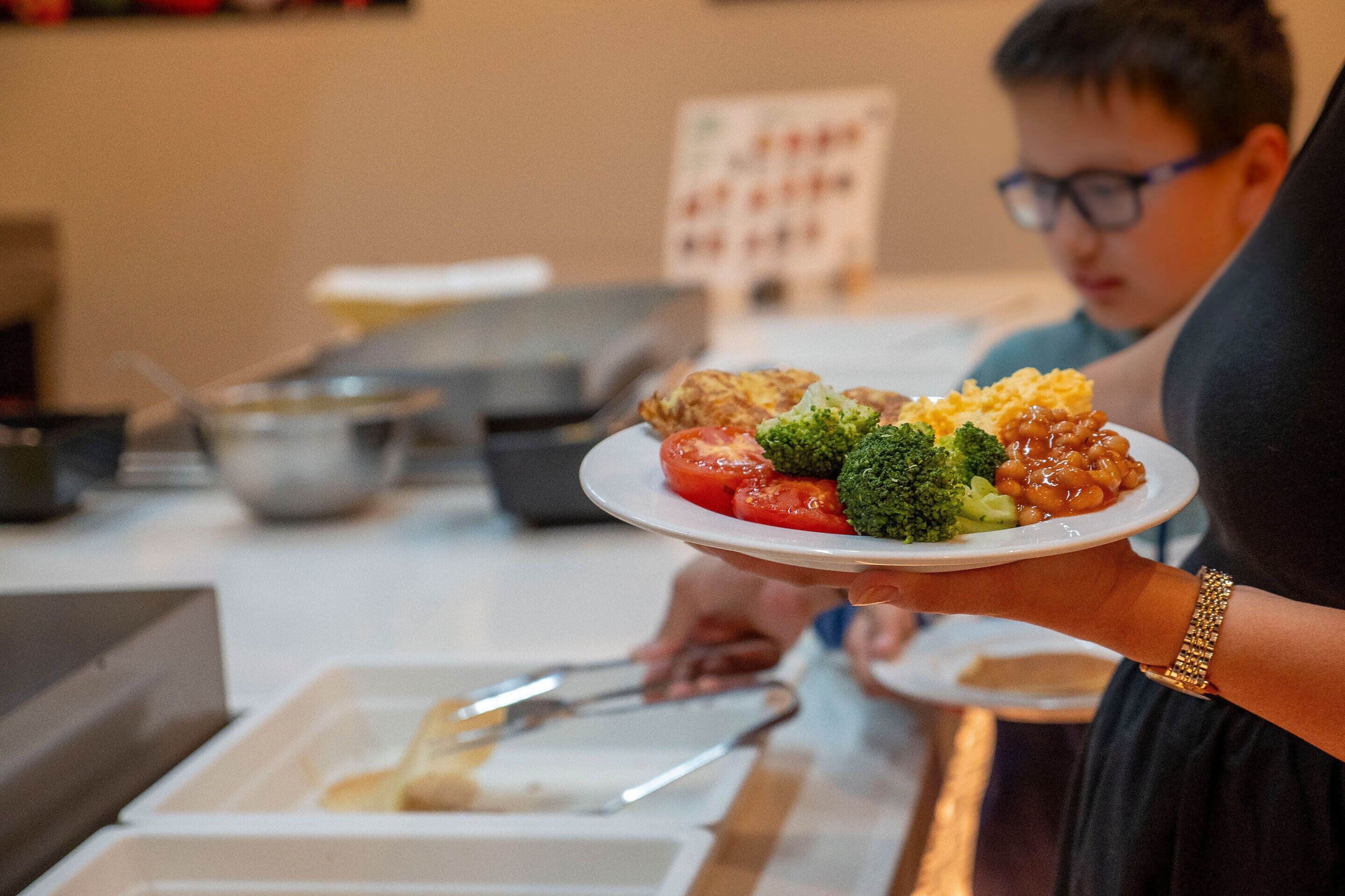 Una persona sosteniendo un plato con comida que incluye tomates, brócoli y frijoles.
